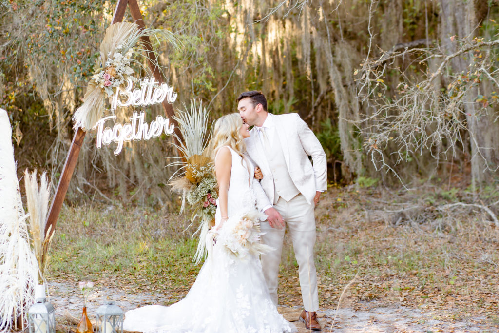 Groom kisses bride in front of triangle arch during their boho elopement