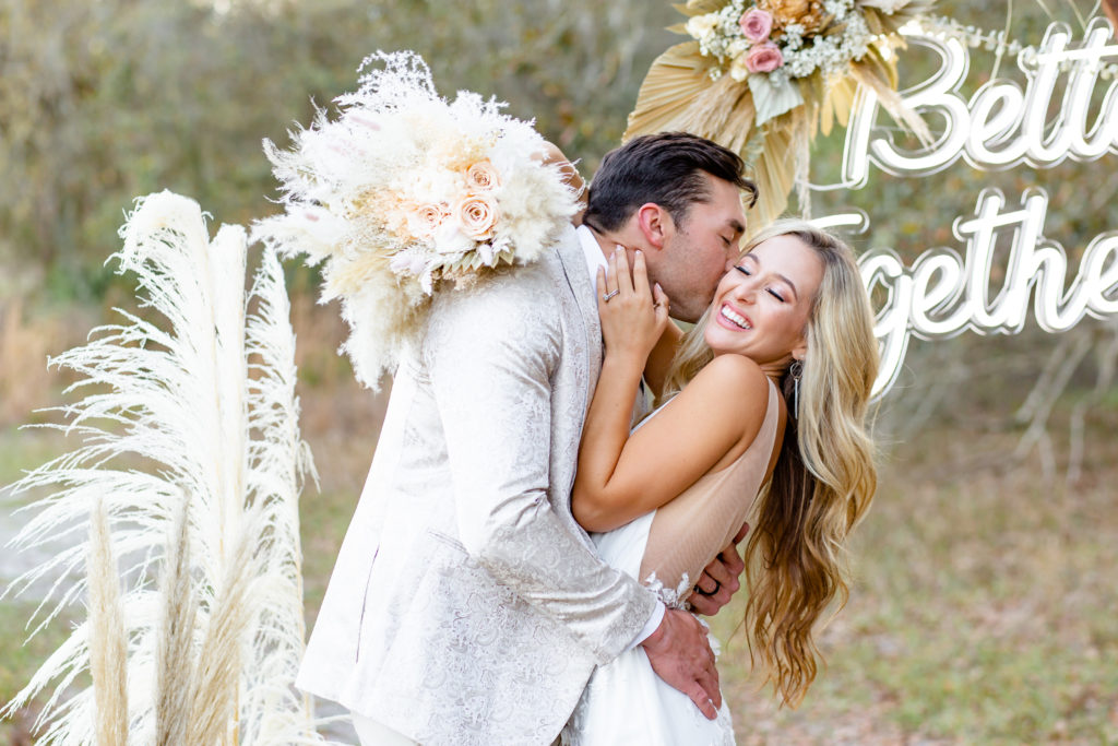 Groom kisses bride while she holds pampas grass bouquet at their Lake Louisa State Park Wedding