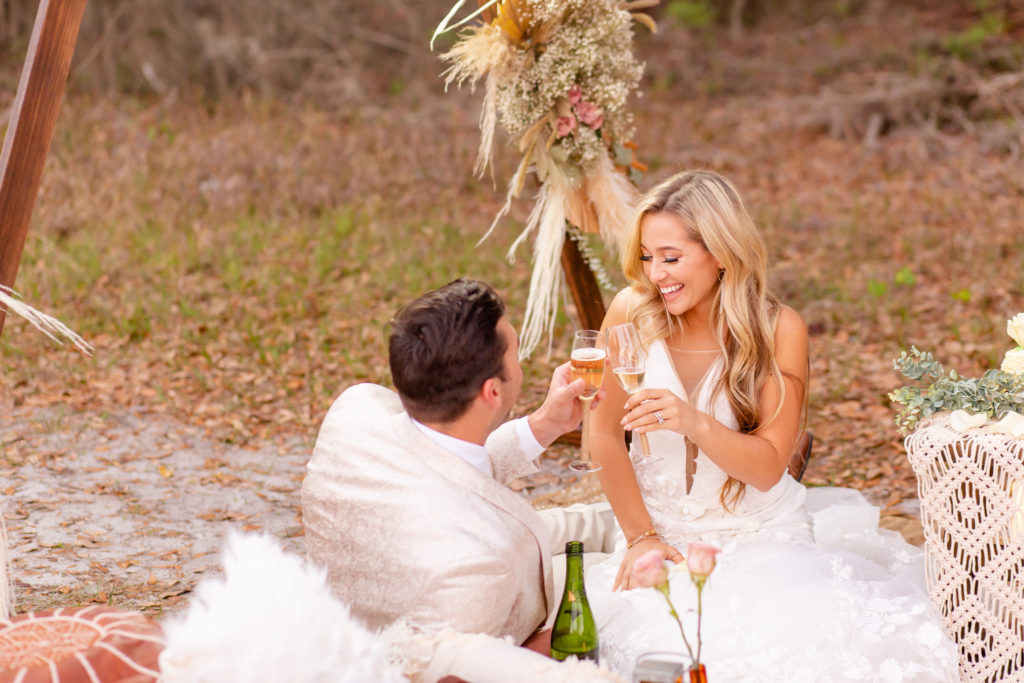 Bride and groom toast with champagne while sitting on a boho styled rug