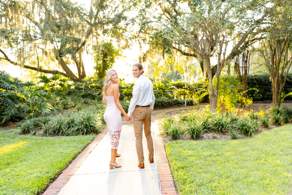 Cypress Grove Park Engagement Photos — couple walks through secluded pathway holding hands with the sun setting behind them