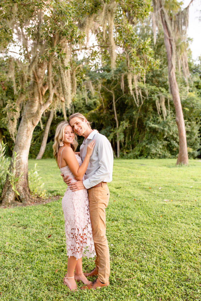Cypress Grove Park Engagement Photos — couple embraces and smiles at the camera while standing on lush, green grass