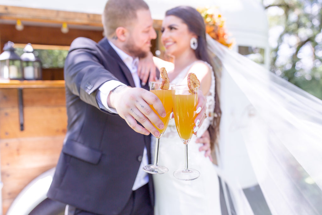 Couple holds citrus wedding cocktails in champagne glasses