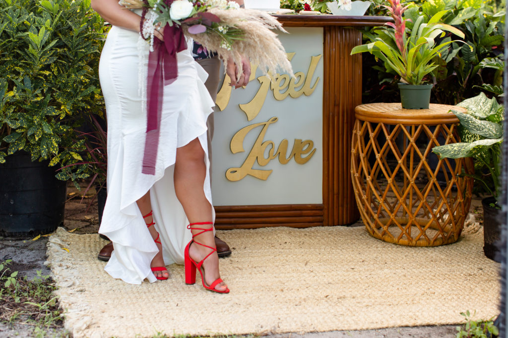 A close-up of a bride's bright red heels standing next to a bar with a sign that says, "I feel love"
