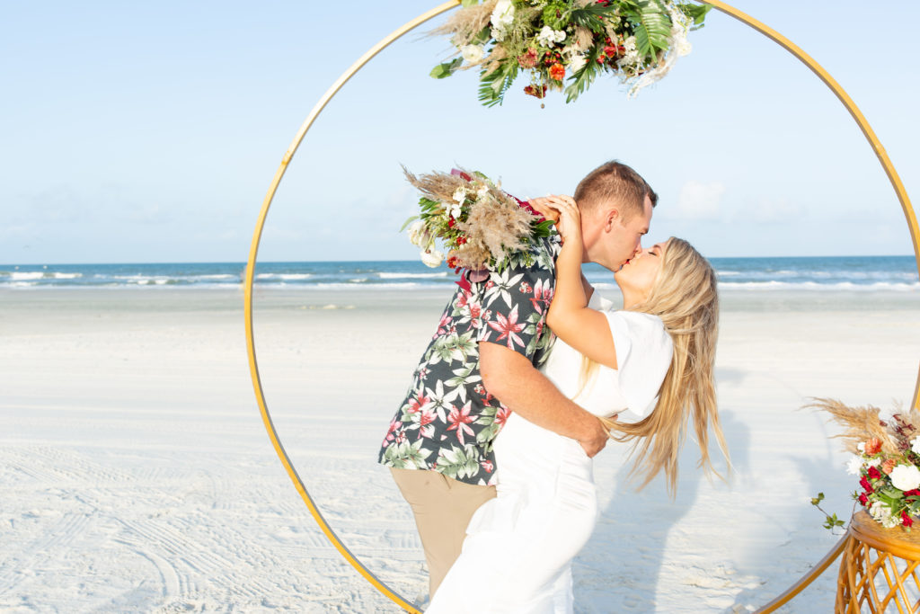 St. Augustine beach wedding photo of the couple kissing in front of a circle arch and tropical attire