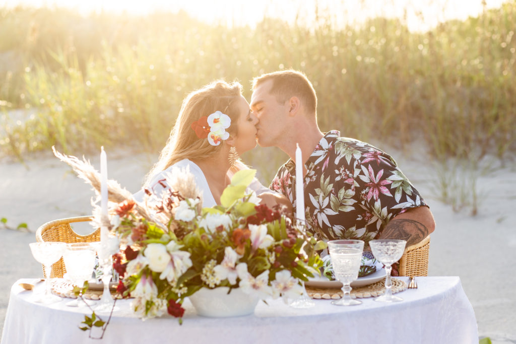 Beach wedding picnic with the couple kissing behind the table