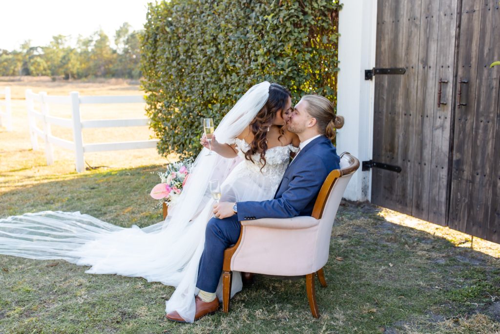 Bramble Tree Estate Wedding Photo — Bride and Groom kissing in pink chairs with champagne