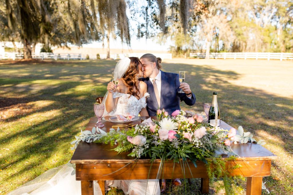 Bramble Tree Estate Wedding Photo — Bride and Groom kissing at sweetheart table under Spanish Moss