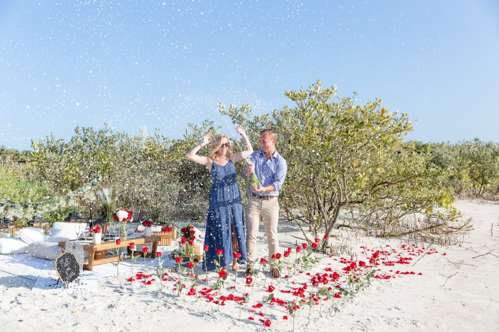 Florida Beach Proposal Photos - New Smyrna Dunes Park Proposal — Surprise Beach proposal with pop up picnic and rose petals on the beach, Couple spraying champagne