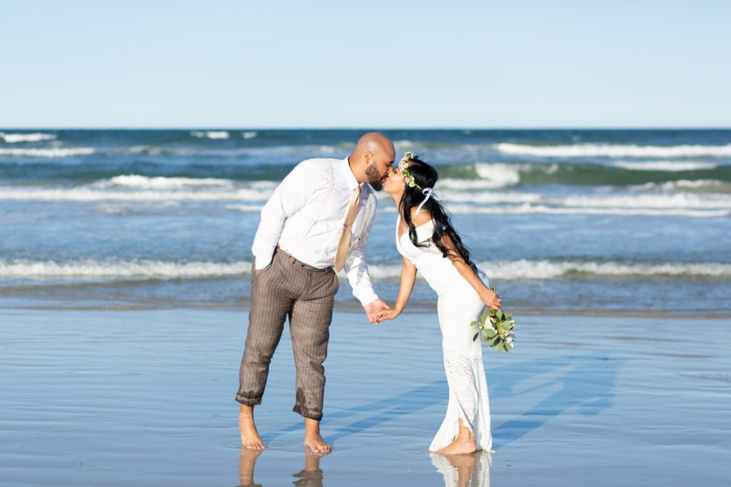 New Smyrna Beach Elopement Photo — Bride and Groom kissing on the beach with bridal bouquet and flower crown