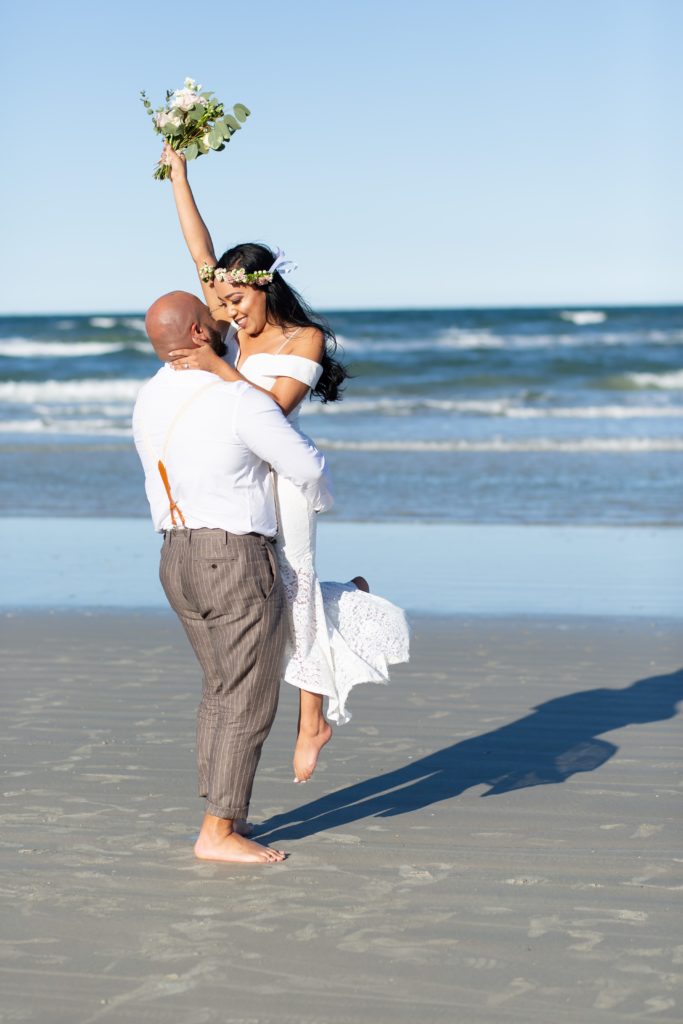 New Smyrna Beach Elopement Photo — Groom picking up Bride holding bouquet and spinning her on the beach