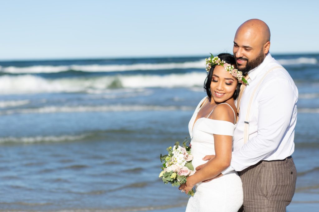 New Smyrna Beach Elopement Photo — Bride with Flower Crown snuggled into Groom on the beach