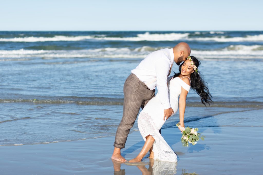 New Smyrna Beach Elopement Photo — Groom dipping Bride on the beach with bridal bouquet and flower crown