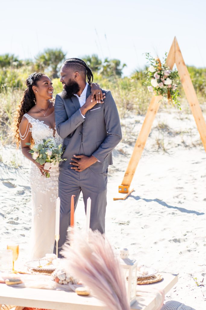 The couple poses together for their Florida beach wedding with a triangle arch in the background