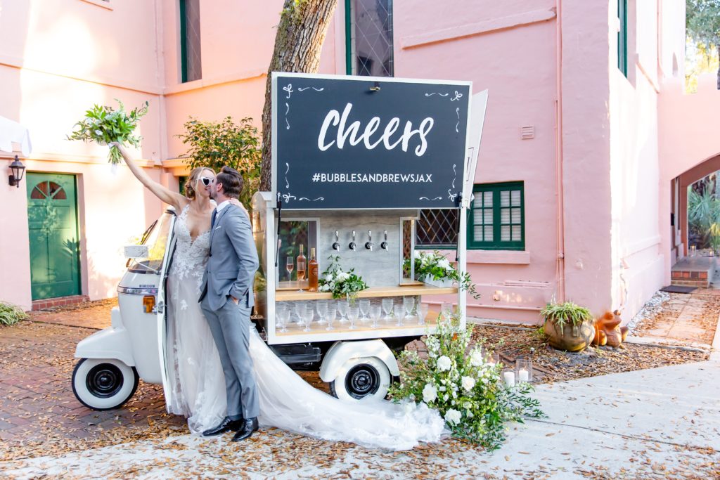 Pillars Castle Wedding Photo — Bride and Groom celebrating at champagne cart in front of pink castle