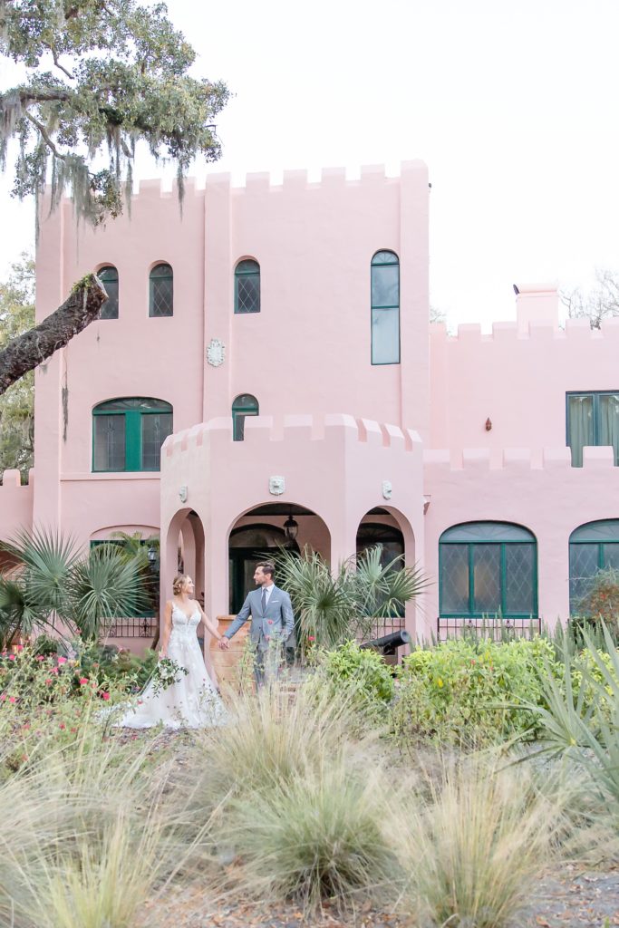 Pillars Castle Wedding Photo — Bride and Groom holding hands in front of pink castle