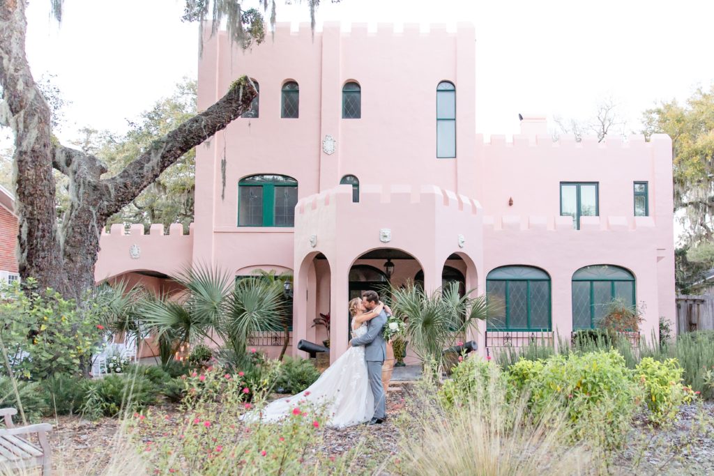 Pillars Castle Wedding Photo — Bride and Groom kissing in front of pink castle