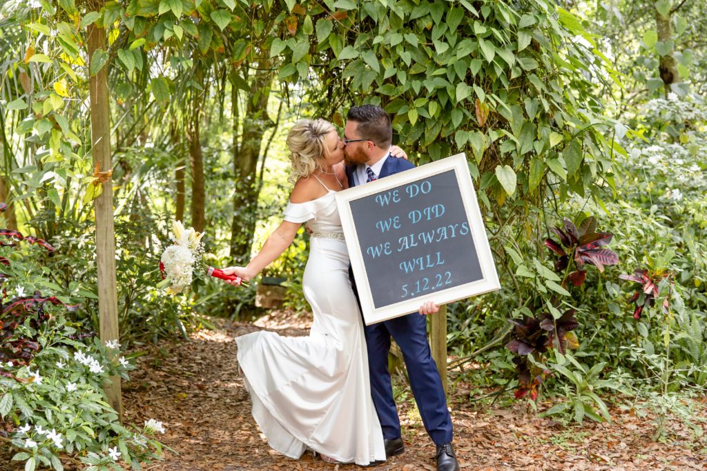 Mead Botanical Garden Elopement Wedding Photo — Bride and Groom kissing under ivy arbor holding sign announcing marriage