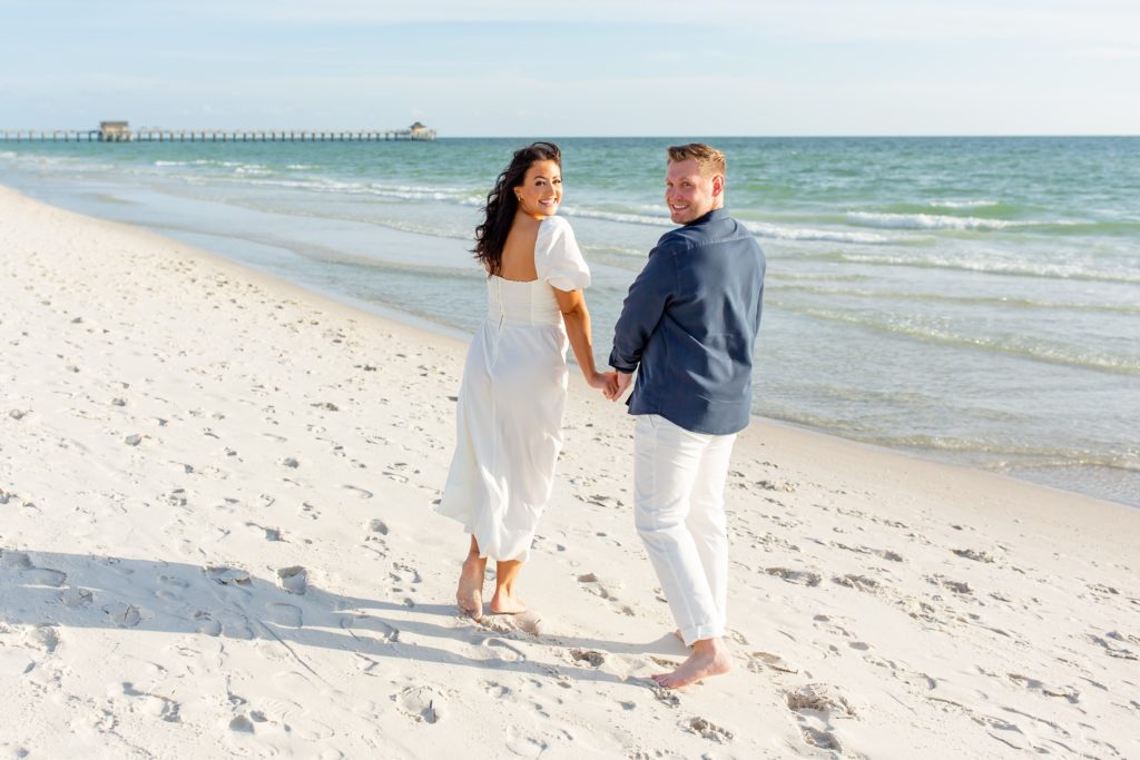 Florida engagement photos — Couple walking in the beach with Naples pier in the background
