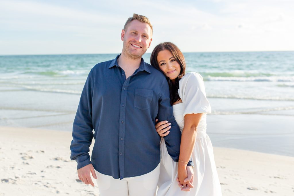 Engagement photo at the beach with the rolling waves behind the couple standing on the shore