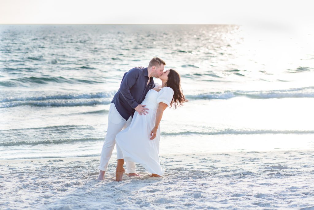 Engagement photo at the beach with the couple kissing just by the water