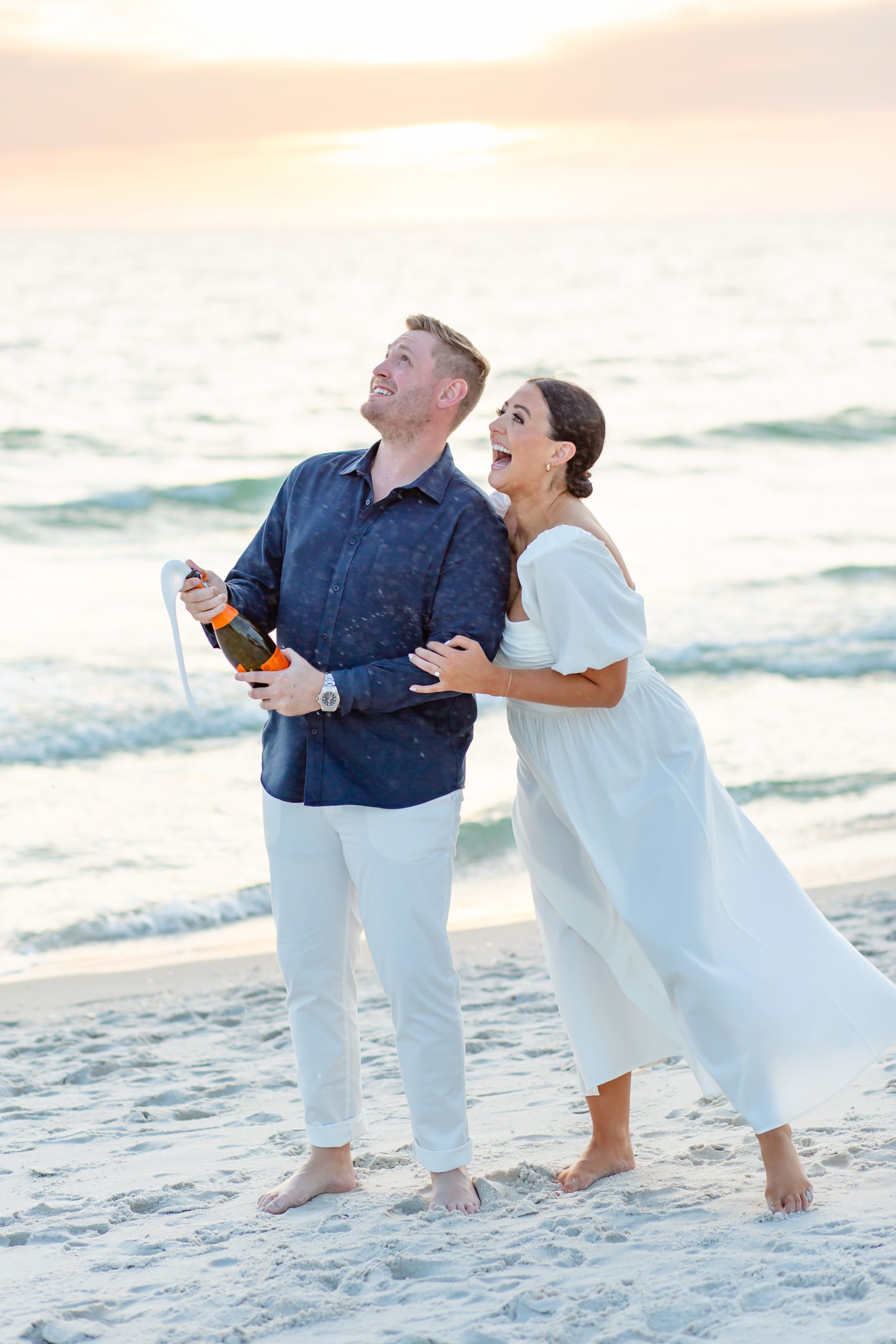 An engaged couple at the beach in Naples pops a glass of champagne