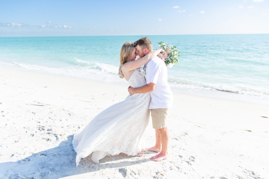 An eloping couple embraces on the beach with the turquoise ocean water behind them