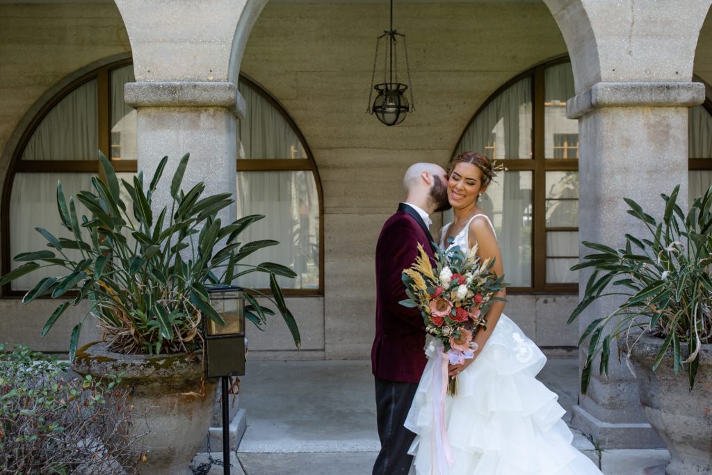 The groom steals a kiss from the bride's cheek in the Lightner Museum courtyard