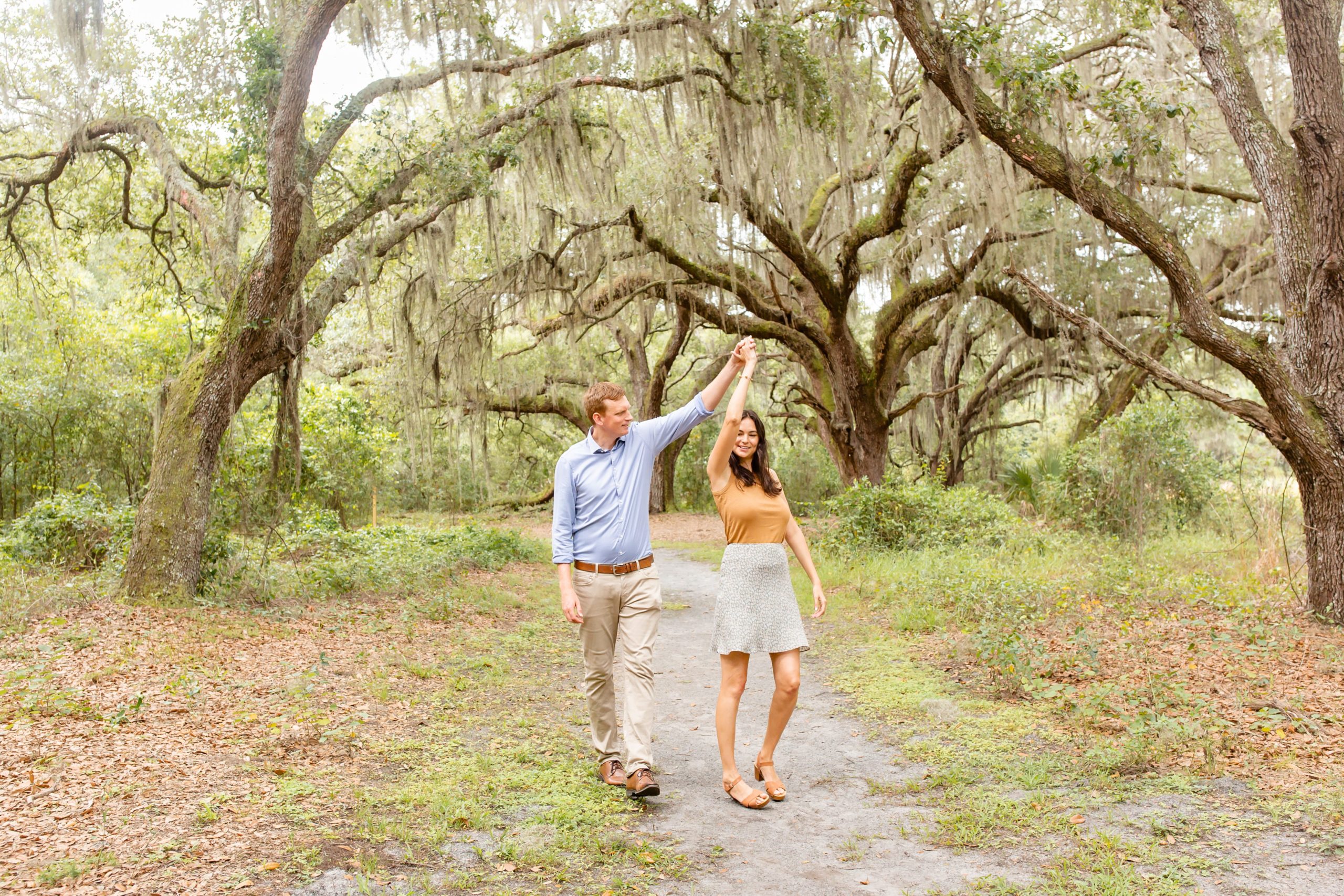 Lake Runnymede Engagement Photo — Guy twirling girl on path of beautiful spanish moss trees