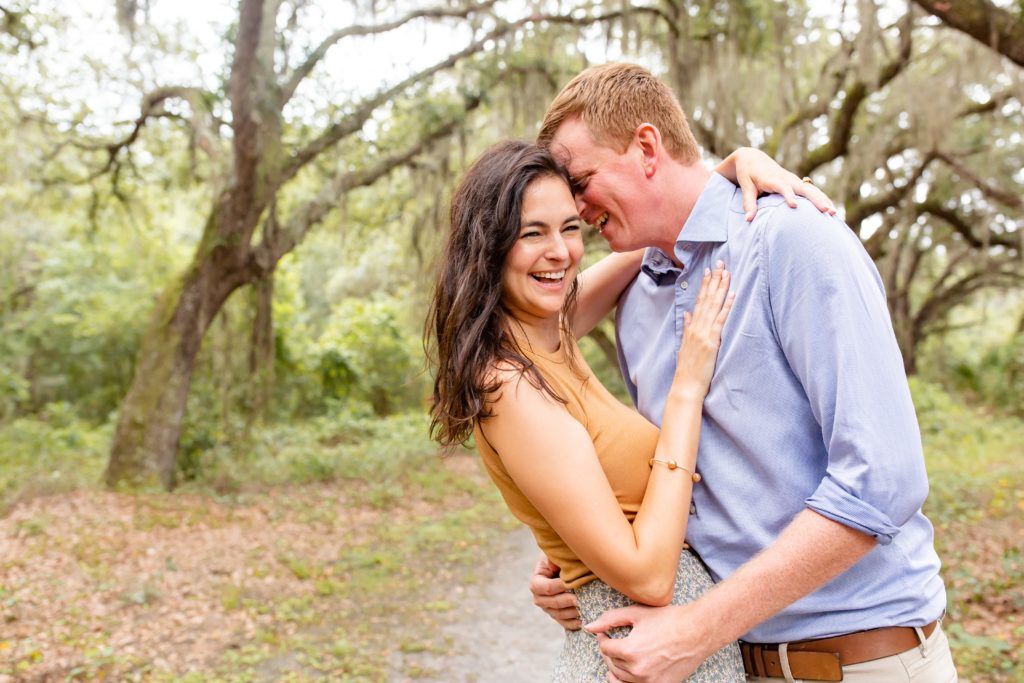 Lake Runnymede Engagement Photo — Girl laughing while guy whispers in her ear on path of beautiful spanish moss trees
