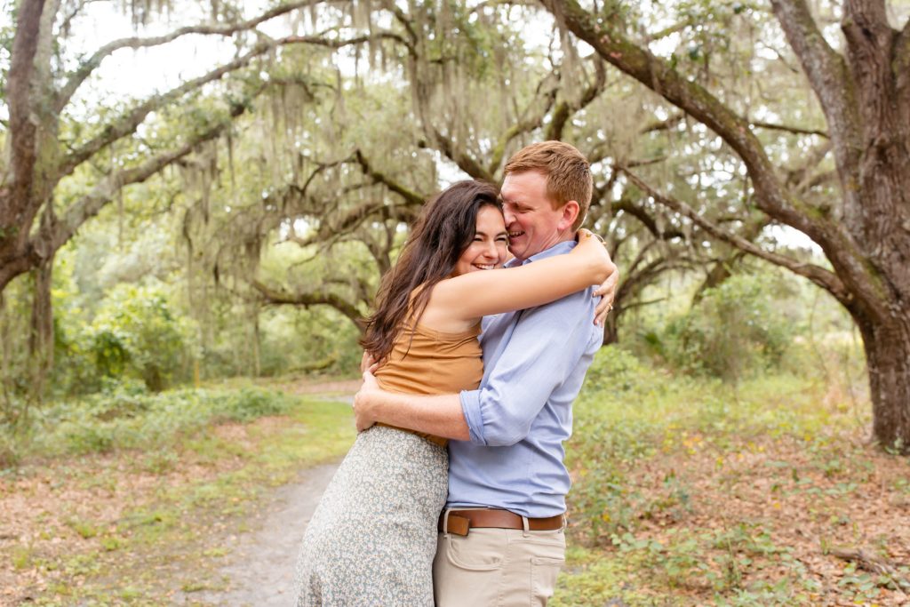 Lake Runnymede Engagement Photo — Guy and girl hugging and laughing on path of beautiful spanish moss trees