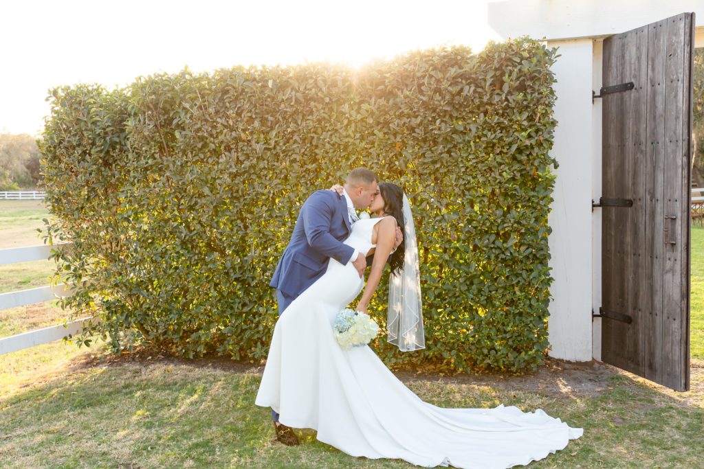 Bramble Tree Estate Wedding in Orlando, FL — 90 Day Fiance Wedding - Groom dipping Bride and kissing her at sunset in front of greenery