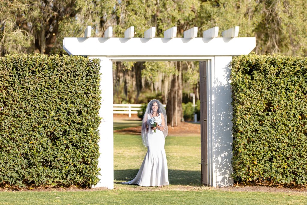 Thaís walking down the aisle underneath a large white arch