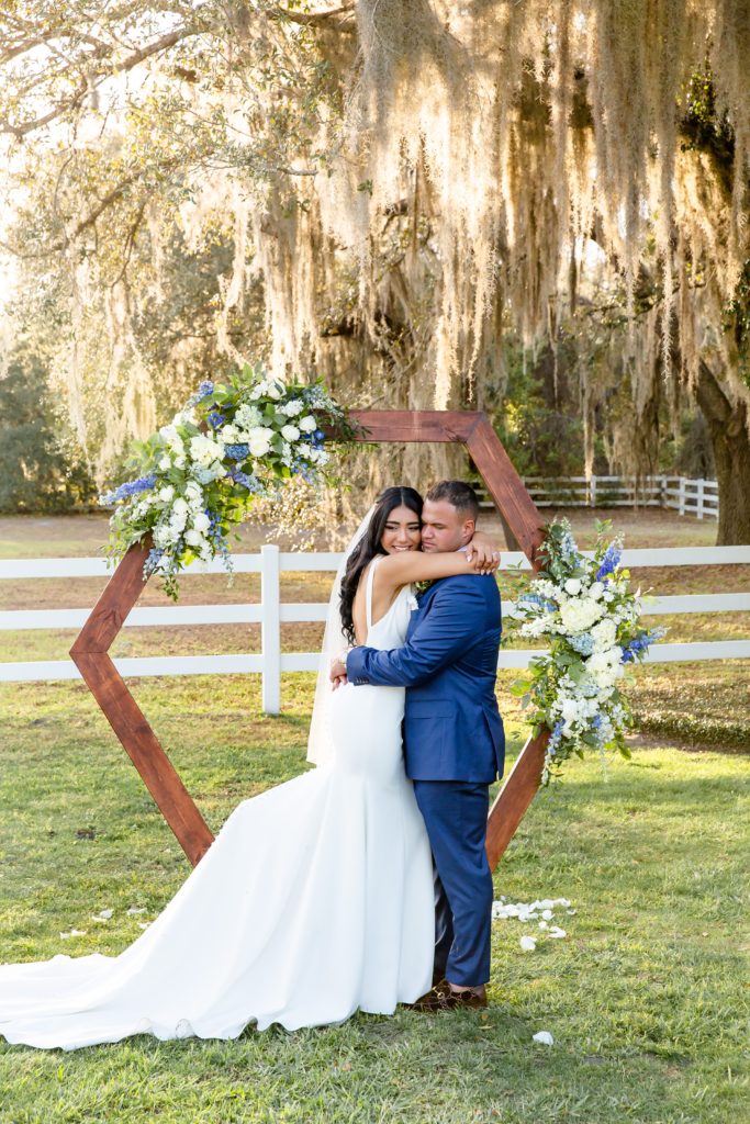 Bramble Tree Estate Wedding in Orlando, FL — 90 Day Fiance Wedding - Bride & Groom hugging at sunset under floral hexagon arch and hanging moss