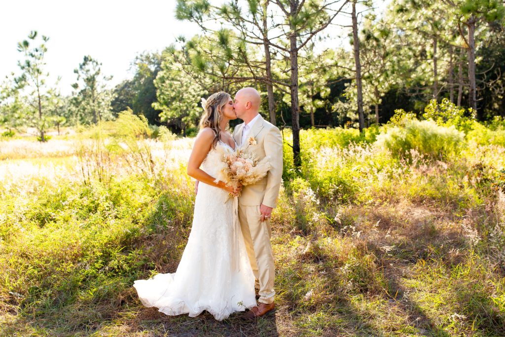 Lake Louisa Wedding Photos in Orlando, FL — Groom and Bride holding a dried floral bridal bouquet kissing in field