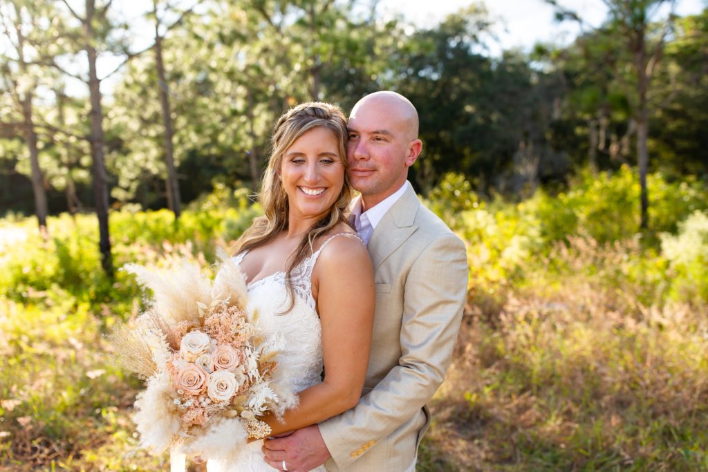 Lake Louisa Wedding Photos in Orlando, FL — Groom and Bride holding a dried floral bridal bouquet standing in field cuddling