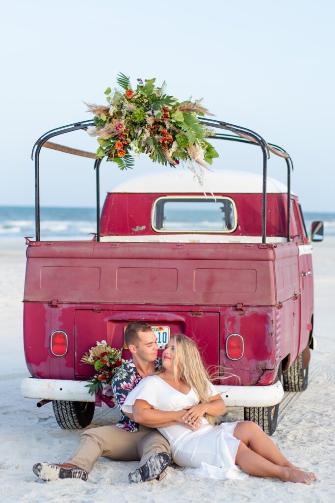 Bride and Groom sit on white sand beach in front of VW van with florals at their elopement on Anastasia Island, St. Augustine