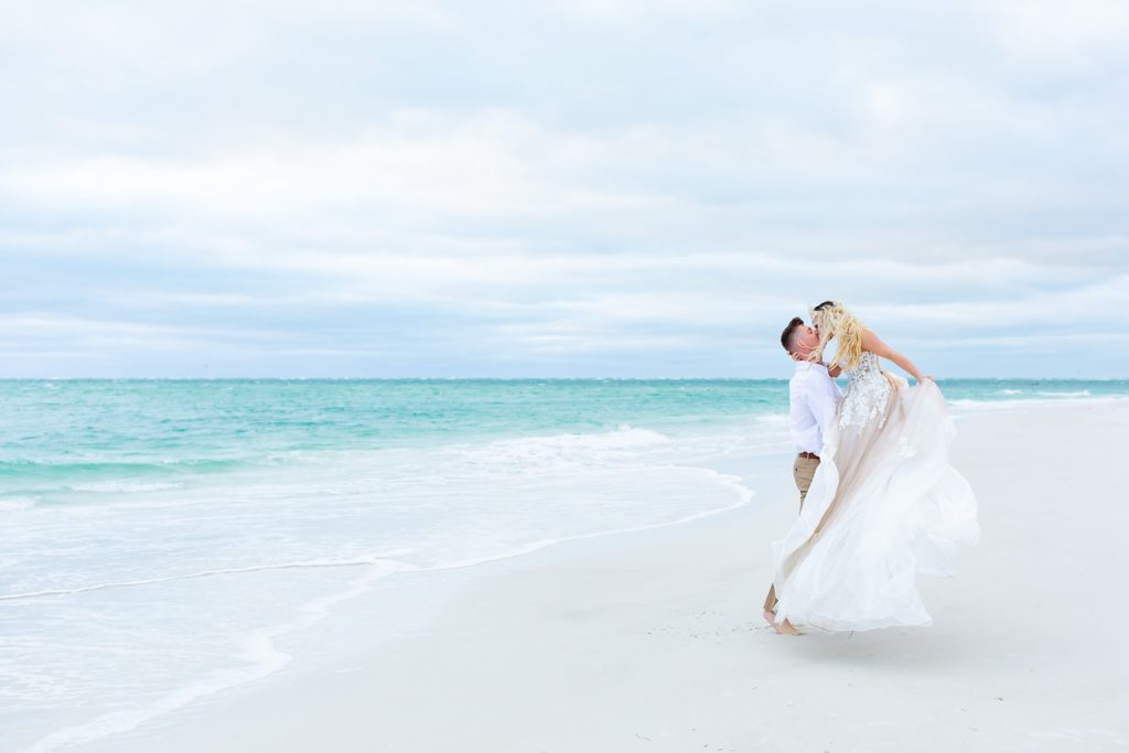 Groom lifting Bride and kissing with beautiful bridal gown at Bean Point Beach on Anna Maria Island