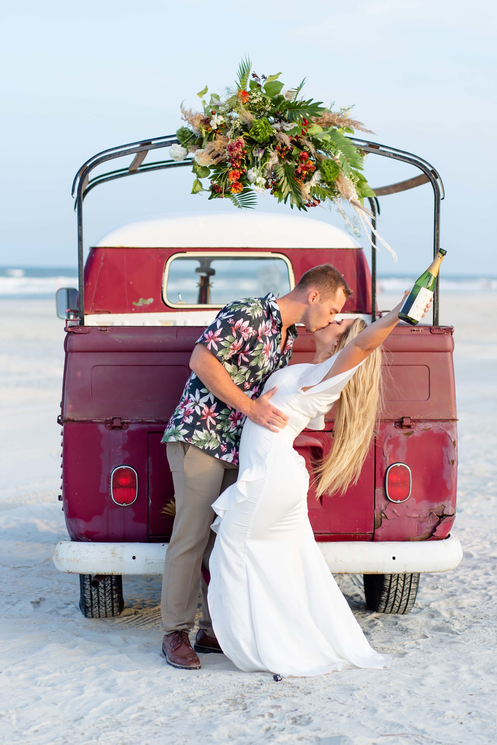 Bride & Groom kissing and toasting champagne in front of VW van with florals on the beach at Anastasia Island, Florida