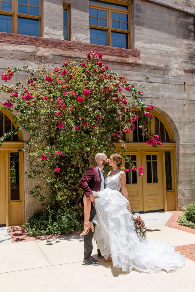 Bride and groom kissing in front of pink flower wall at the Lightner Museum in St. Augustine, FL