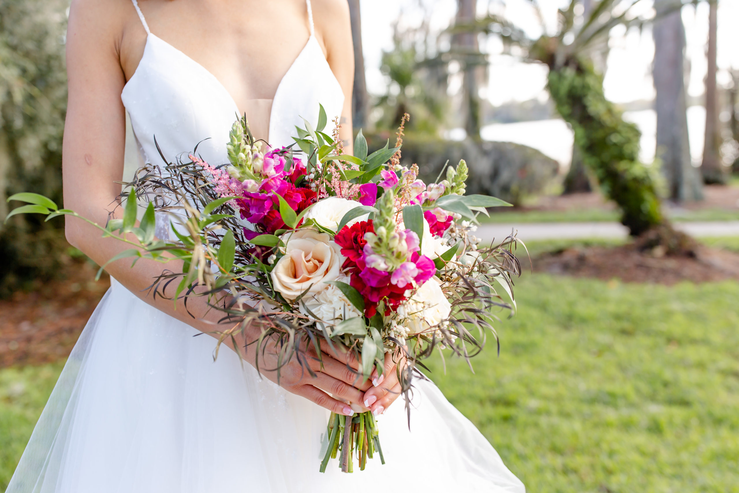 Fuchsia and Cream Bridal Bouquet held by bride wearing wedding gown with straps at Cypress Grove Estate