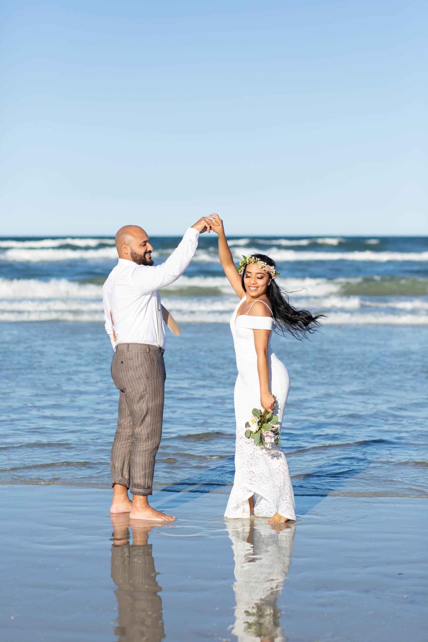 Groom twirling bride in ocean with bride wearing floral crown and petite bridal bouquet in New Smyrna Beach, FL