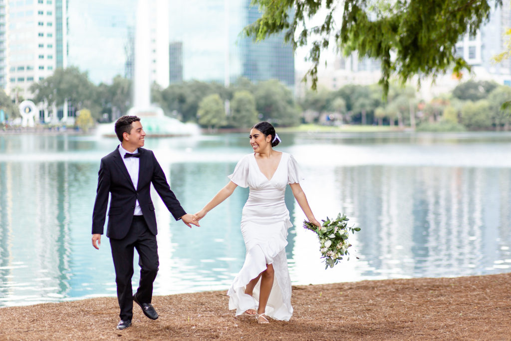 Bride & Groom holding hands and running in front of fountain at Lake Eola Park in Orlando, FL