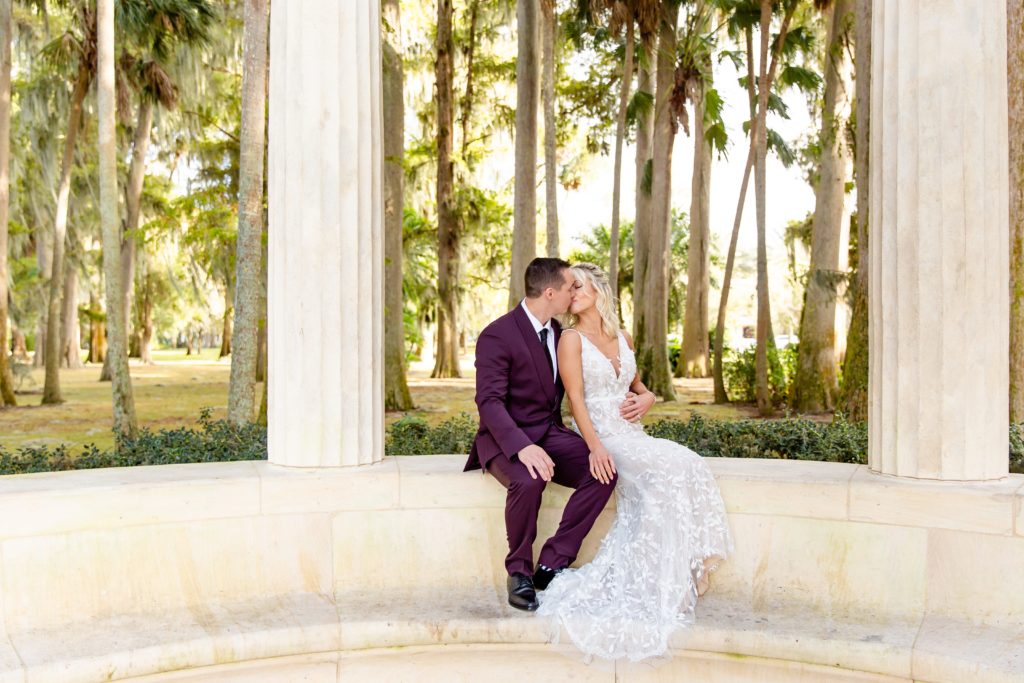 Bride and Groom kissing while sitting on exedra at Kraft Azalea Gardens in Orlando