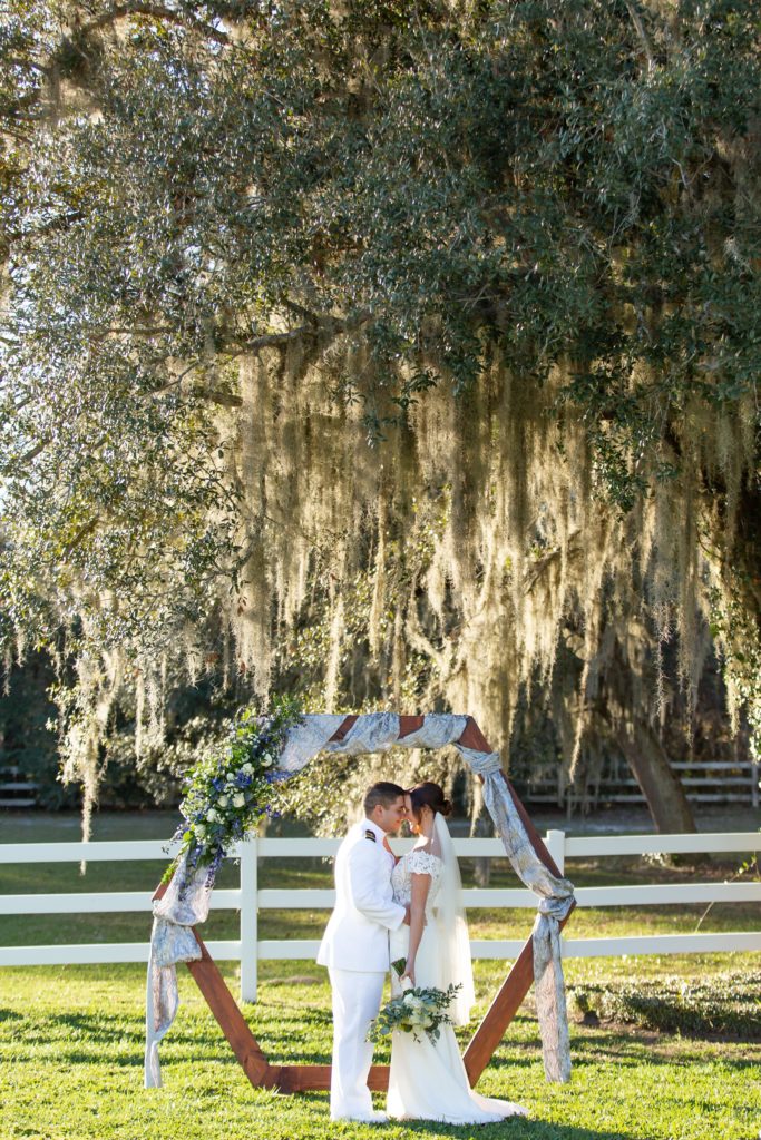 Bride and Groom standing under beautiful live oak tree at sunset in front of wedding arch while forehead to forehead for their micro wedding at Bramble Tree Estate in Orlando, Florida