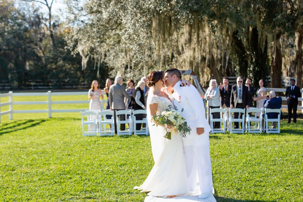Bride and Groom kissing as guests watch with beautiful live oak tree backdrop after intimate wedding at Bramble Tree Estate in Orlando, Florida