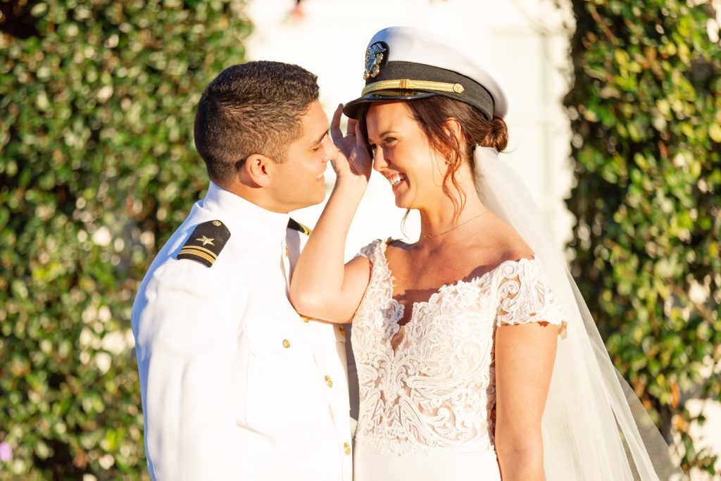 Bride wearing Groom's Navy hat and smiling at him at sunset standing under ivy arch at Bramble Tree Estate in Orlando, Florida