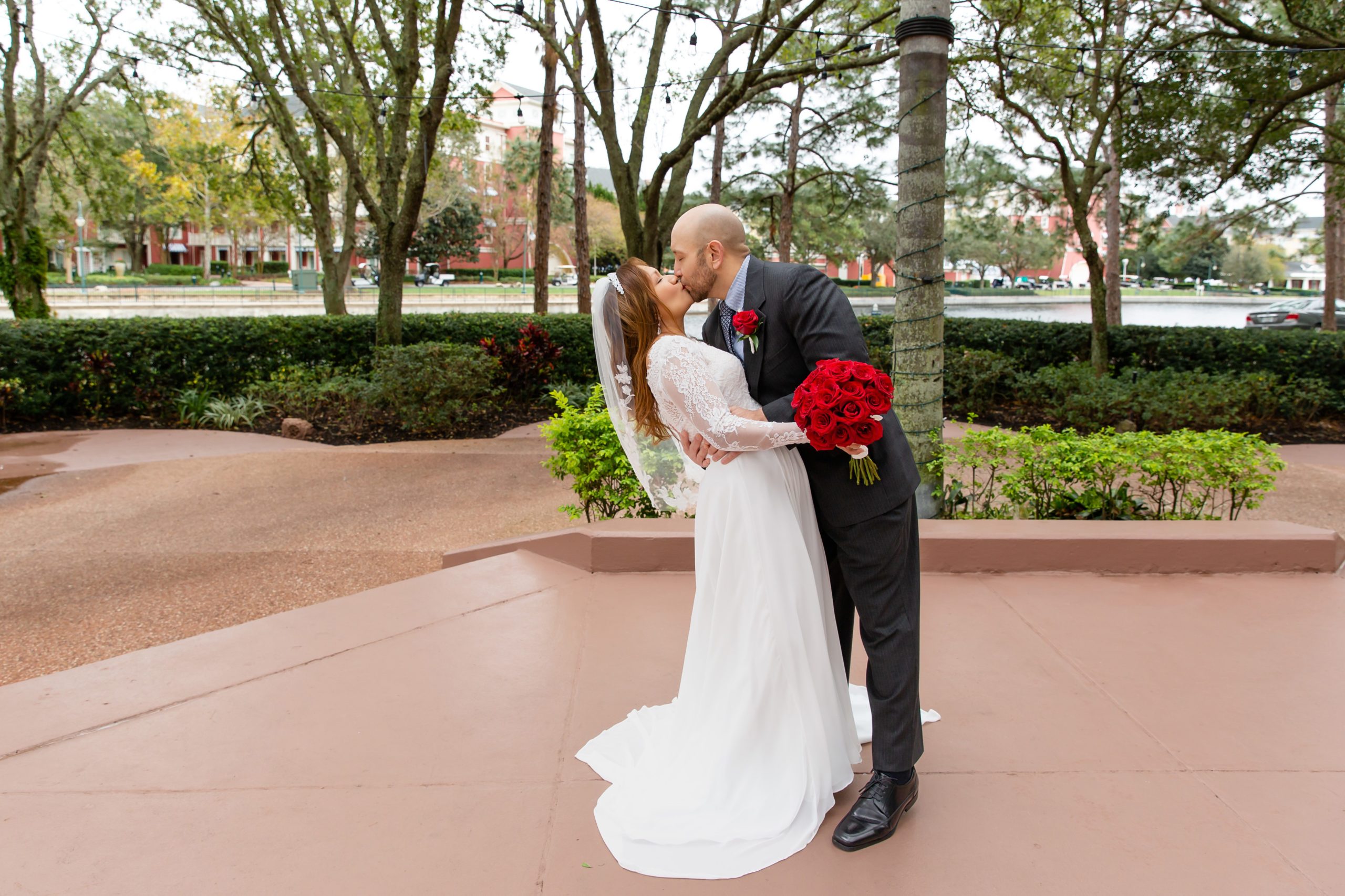 Groom dipping Bride and kissing with red rose bouquet after eloping at Disney Swan Resort in Orlando, FL