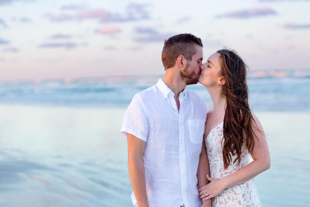 New Smyrna Beach Engagement Photo — Couple kissing on the beach at sunset with cotton candy skies