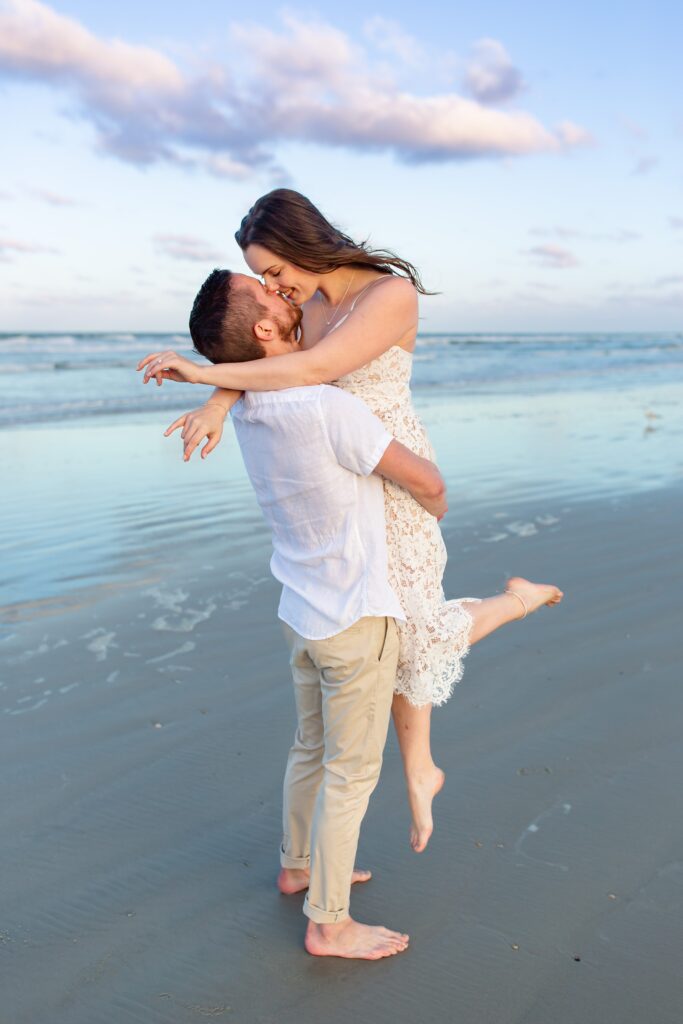 New Smyrna Beach Engagement Photo — Guy lifting girl and kissing on the beach at sunset
