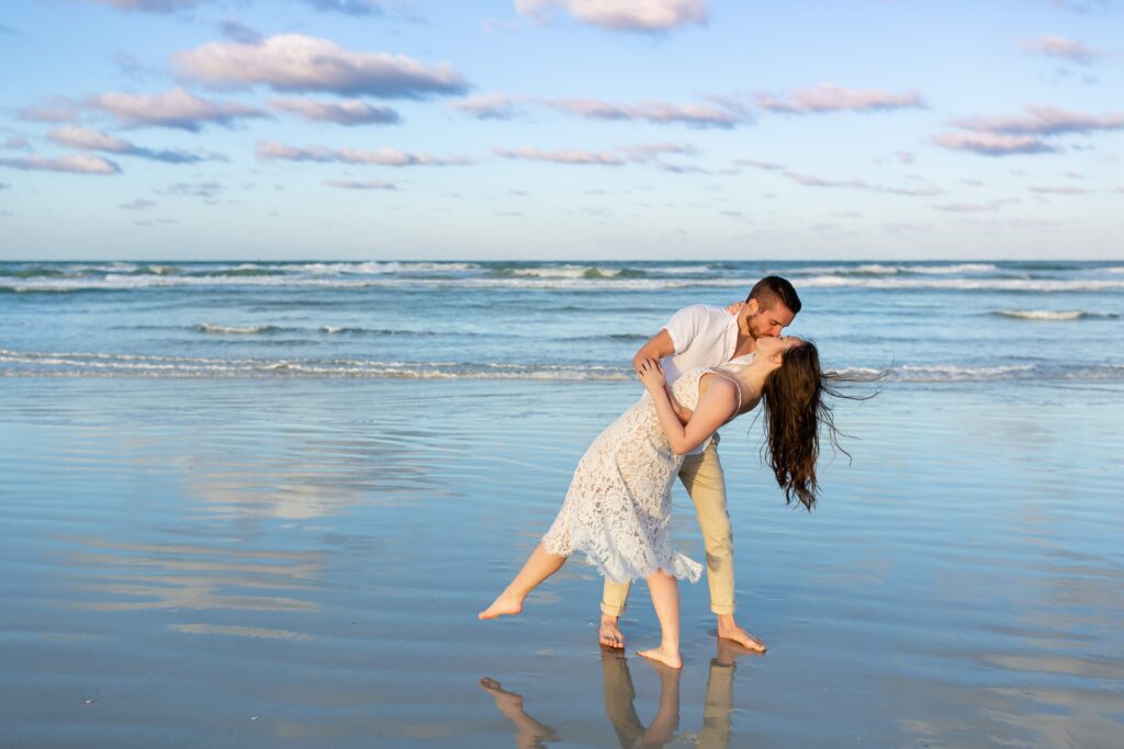 New Smyrna Beach Engagement Photo — Guy dipping girl and kissing her on the beach at sunset